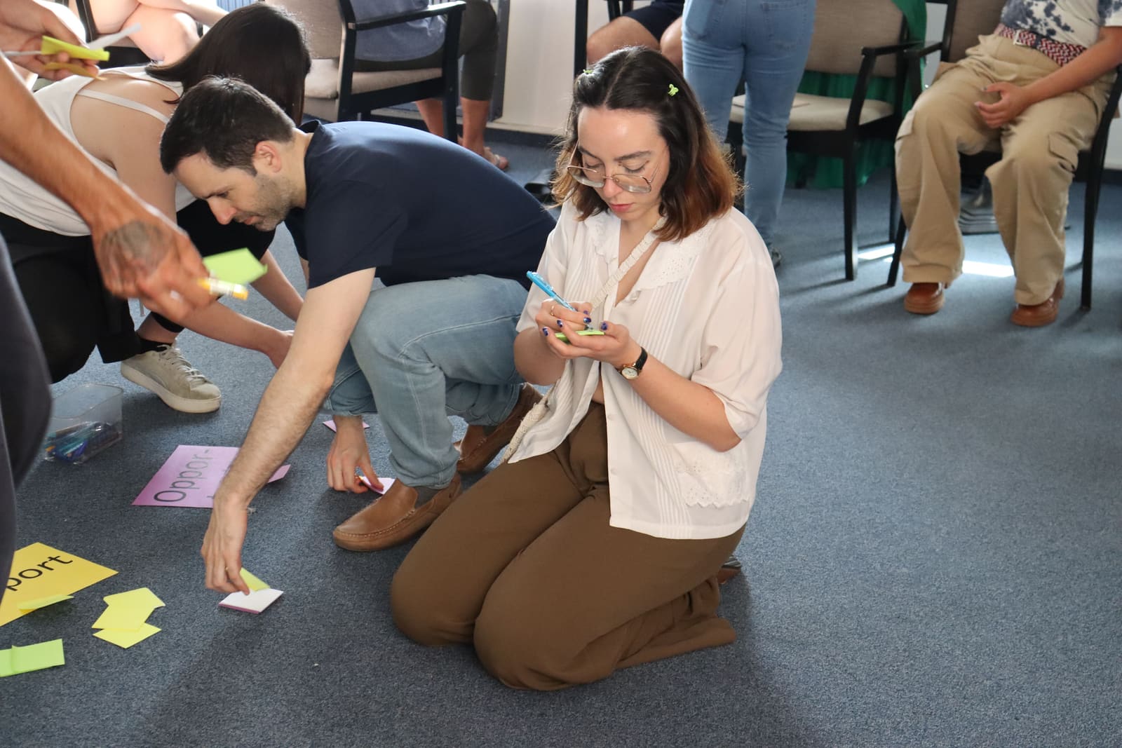 Sessão prática de uma mobilidade Erasmus+: participantes ajoelhados no chão a escrever em post-its e a organizar cartões coloridos.